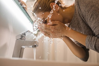 A view from below of a lady stood over a sink with a silver tap washing her face.