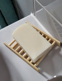 Bar of soap on soap rack on sink with grey tiled background and green towel hanging on wall